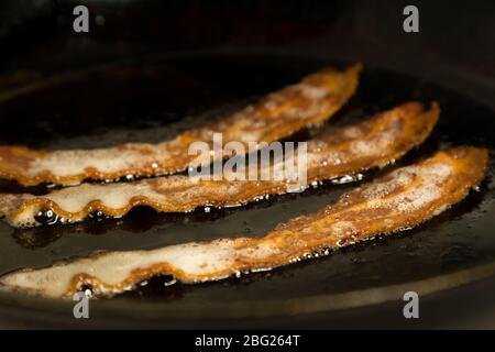 Primo piano di alcune gustose strisce di pancetta frittura in una padella. Foto Stock