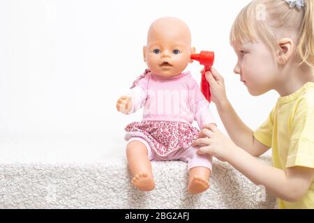 Una bambina gioca con una bambola esamina le sue orecchie. Il concetto di otolaringologia pediatrica in medicina, il trattamento dell'otite media e dei tappi di zolfo in c Foto Stock