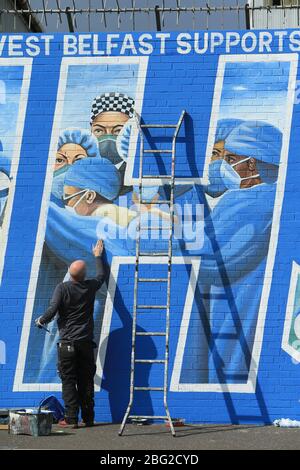 BELFAST 18/04/2020. Gli artisti di Belfast occidentale del West Belfast Festival hanno messo i tocchi finali di un nuovo murale che sostiene i lavoratori del NHS sulla International Peacewall on the Falls Road, a ovest di Belfast, durante questo blocco Covid-19 a Belfast, Irlanda del Nord. Sono state registrate 17 morti che hanno portato il numero di morti a 193 annunciato dall'Agenzia per la sanità pubblica. Foto/Paul McErlane Foto Stock