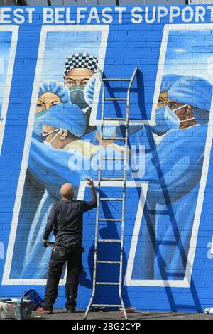 BELFAST 18/04/2020. Gli artisti di Belfast occidentale del West Belfast Festival hanno messo i tocchi finali di un nuovo murale che sostiene i lavoratori del NHS sulla International Peacewall on the Falls Road, a ovest di Belfast, durante questo blocco Covid-19 a Belfast, Irlanda del Nord. Sono state registrate 17 morti che hanno portato il numero di morti a 193 annunciato dall'Agenzia per la sanità pubblica. Foto/Paul McErlane Foto Stock