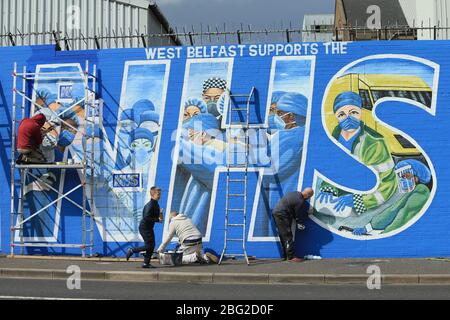 BELFAST 18/04/2020. Gli artisti di Belfast occidentale del West Belfast Festival hanno messo i tocchi finali di un nuovo murale che sostiene i lavoratori del NHS sulla International Peacewall on the Falls Road, a ovest di Belfast, durante questo blocco Covid-19 a Belfast, Irlanda del Nord. Sono state registrate 17 morti che hanno portato il numero di morti a 193 annunciato dall'Agenzia per la sanità pubblica. Foto/Paul McErlane Foto Stock