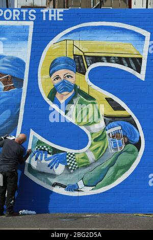 BELFAST 18/04/2020. Gli artisti di Belfast occidentale del West Belfast Festival hanno messo i tocchi finali di un nuovo murale che sostiene i lavoratori del NHS sulla International Peacewall on the Falls Road, a ovest di Belfast, durante questo blocco Covid-19 a Belfast, Irlanda del Nord. Sono state registrate 17 morti che hanno portato il numero di morti a 193 annunciato dall'Agenzia per la sanità pubblica. Foto/Paul McErlane Foto Stock