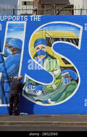 BELFAST 18/04/2020. Gli artisti di Belfast occidentale del West Belfast Festival hanno messo i tocchi finali di un nuovo murale che sostiene i lavoratori del NHS sulla International Peacewall on the Falls Road, a ovest di Belfast, durante questo blocco Covid-19 a Belfast, Irlanda del Nord. Sono state registrate 17 morti che hanno portato il numero di morti a 193 annunciato dall'Agenzia per la sanità pubblica. Foto/Paul McErlane Foto Stock