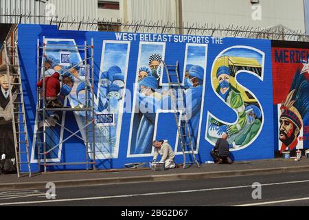 BELFAST 18/04/2020. Gli artisti di Belfast occidentale del West Belfast Festival hanno messo i tocchi finali di un nuovo murale che sostiene i lavoratori del NHS sulla International Peacewall on the Falls Road, a ovest di Belfast, durante questo blocco Covid-19 a Belfast, Irlanda del Nord. Sono state registrate 17 morti che hanno portato il numero di morti a 193 annunciato dall'Agenzia per la sanità pubblica. Foto/Paul McErlane Foto Stock