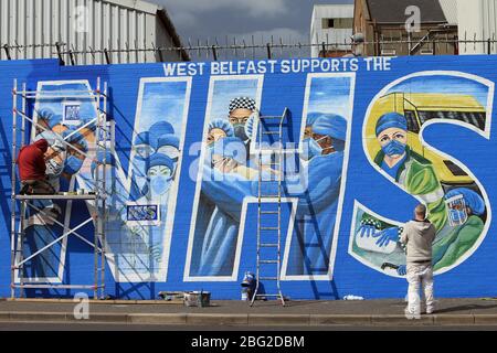 BELFAST 18/04/2020. Gli artisti di Belfast occidentale del West Belfast Festival hanno messo i tocchi finali di un nuovo murale che sostiene i lavoratori del NHS sulla International Peacewall on the Falls Road, a ovest di Belfast, durante questo blocco Covid-19 a Belfast, Irlanda del Nord. Sono state registrate 17 morti che hanno portato il numero di morti a 193 annunciato dall'Agenzia per la sanità pubblica. Foto/Paul McErlane Foto Stock