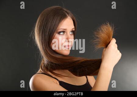 Bella donna che tiene le estremità divise dei suoi capelli lunghi, su sfondo nero Foto Stock