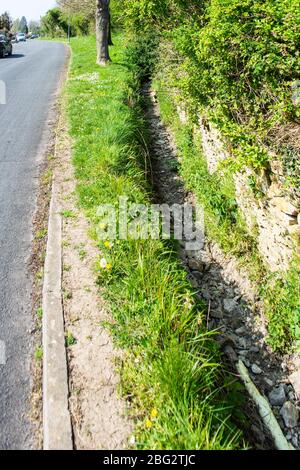 Un canale di drenaggio asciutto e vuoto che si riempie di acqua quando c'è un periodo di tempo bagnato Foto Stock