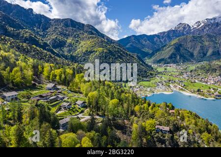 L'improbabile paesaggio aereo del paese Molveno, Italia, acque azzurre del lago, spiaggia vuota, montagne innevate Dolomiti sullo sfondo, tetto Foto Stock