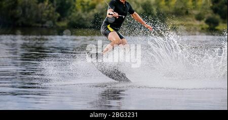 wakeboarder equitazione sul lago dietro barca in spruzzi d'acqua Foto Stock