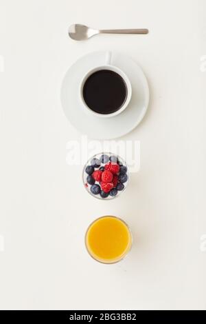 Vista dall'alto con una composizione minima di deliziosi dessert decorati con bacche fresche accanto alla tazza da caffè su sfondo bianco, concetto di colazione, copia spac Foto Stock