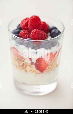Primo piano verticale di una deliziosa tazza di parfait yogurt con bacche fresche e granola isolata su sfondo bianco Foto Stock