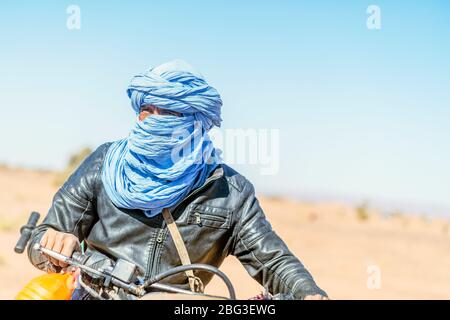 Mhamid, Marocco - 17 marzo 2020: Sorprendente ritratto di beduino uomo sulla sua moto che guida attraverso il deserto del Sahara. Foto Stock
