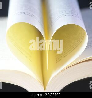 pagine di libro a forma di cuore quadrato, fuoco selettivo su un concetto di fondo nero dell'amore di lettura Foto Stock