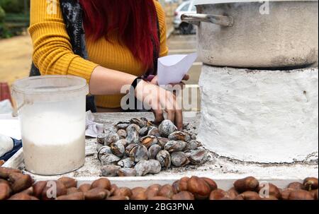 Donna che raccoglie castagne arrostite in una stalla di strada, Siviglia, Spagna Foto Stock