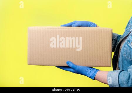 Consegna sicura. Primo piano donna mani in guanti con scatola di cartone. Concetto anti-Coronavirus. Mock Up. Foto Stock