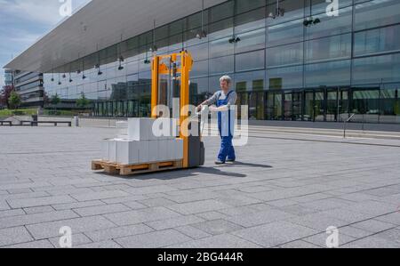 uomo in tuta aziona un impilatore elettrico carico di scatole Foto Stock