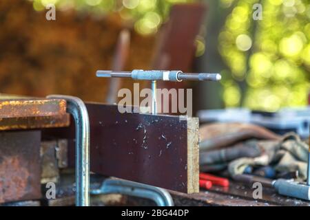 Lavoratore in guanti protettivi gialli e blu tagliare il filo interno con un rubinetto a mano. Preparazione di un prodotto metallico per la giunzione mediante filettatura manuale Foto Stock