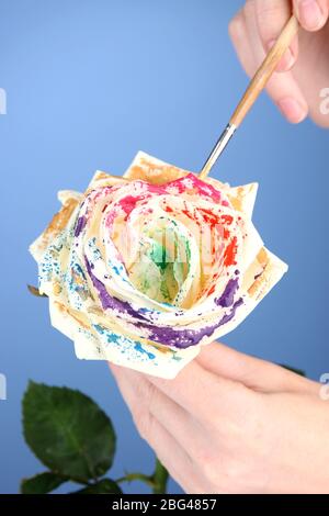 Le mani femminili tengono il fiore bianco e lo dipingono con i colori, su sfondo colorato Foto Stock