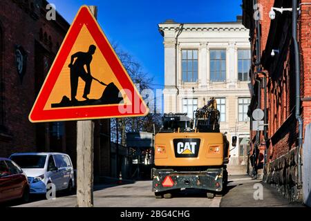 La strada funziona segnaletica stradale per strada in città in una giornata di sole con l'escavatore idraulico Cat sullo sfondo. Helsinki, Finlandia. Aprile 19, 2020. Foto Stock