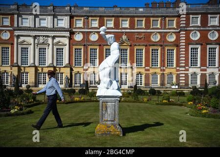 Il responsabile operativo di Gardens and Estates Graham Dillamore cammina davanti a una statua avvolta di Bacchus nel Giardino privato all'Hampton Court Palace, nel sud-ovest di Londra, che è stato temporaneamente chiuso mentre il Regno Unito rimane in blocco durante la pandemia di coronavirus. Foto Stock