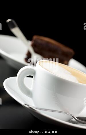 Una tazza di delizioso caffe latte fresco con torta al cioccolato sullo sfondo. Foto Stock