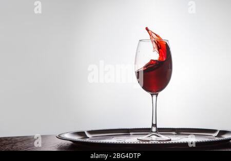 il vino rosso fuoriesce da un bicchiere che rimane sul tavolo di legno Foto Stock