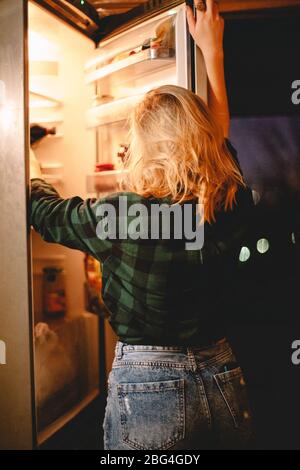 Giovane donna affamata in cerca di cibo in frigorifero di notte a casa Foto Stock