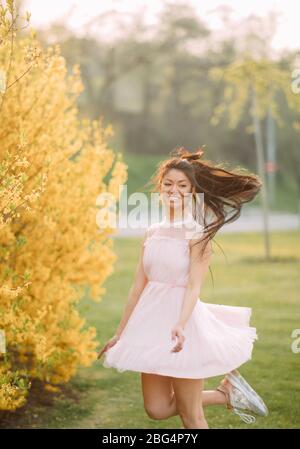 Giovane donna in abito bianco ha godere e si rilassa nel parco con cespugli fioriti di forsitia. Foto Stock