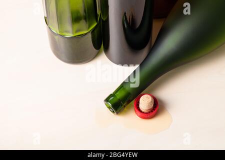 vista dall'alto della bottiglia di cognac rovesciata e del sughero in liquido versato vicino a bottiglie di vino vuote su tavola di legno Foto Stock