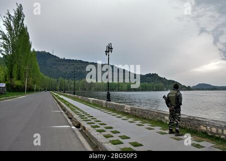 Un trooper paramilitare si trova guardia lungo la riva del lago dal durante un blocco nazionale.il blocco imposto per aiutare a combattere la diffusione di pandemia coronavirus nella valle del Kashmir è stato esteso fino al 03 maggio 2020. Il numero di casi COVID-19 in Jammu e Kashmir è salito a 354, mentre altre quattro persone hanno provato positivo per il virus, ha detto lunedì. Foto Stock