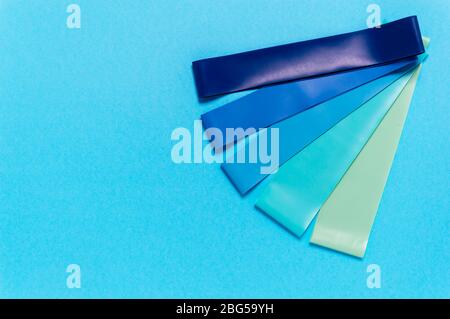 Set di elastici elastici in gomma resistenti in blu, turchese e verde su sfondo blu. Attrezzature per lo sport o l'allenamento a casa. Fitness e riabilitazione Foto Stock