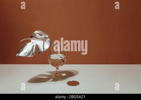 Foglio d'argento di una monstera in vaso su uno sfondo di terracotta parete. Design di tendenza. Minimalismo pastello. Spazio di copia Foto Stock