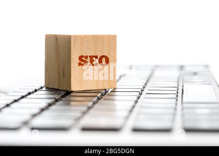 SEO concetto con la parola scritta su un blocco di legno che giace su una tastiera del computer concettuale di ottimizzazione del sito web, copyspace su bianco dietro. Foto Stock