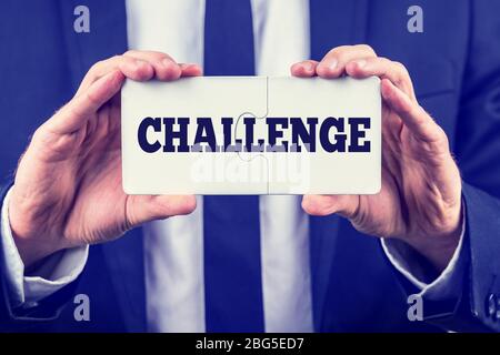 Uomo che tiene in mano due pezzi di puzzle interbloccati con la parola sfida, mentre dimostra che c'è una soluzione e una risposta e un modo per il successo, Foto Stock