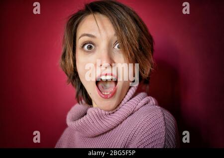 Ritratto ravvicinato di giovane donna emozionale con capelli corti vestiti con maglione rosa sta posando in studio su sfondo rosa brillante Foto Stock