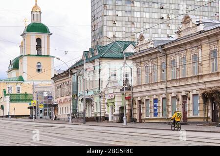 Perm, Russia - 19 aprile 2020: Il servizio di consegna di cibo on-line del corriere guida una bicicletta su una strada vuota durante lo scoppio del COVID-19 Foto Stock