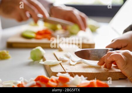 Le mani di una ragazza e suo padre tagliano le verdure per cucinare Foto Stock