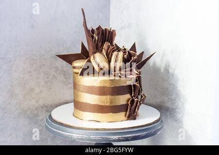 Torta di compleanno al cioccolato con strisce dorate, decorazione al cioccolato fondente e macaroon. Foto Stock