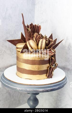 Torta di compleanno al cioccolato con strisce dorate, decorazione al cioccolato fondente e macaroon. Foto Stock
