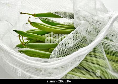 Fagioli verdi in una borsa a rete di prodotti alimentari sostenibile. Verdure in imballaggi riutilizzabili ecologici su sfondo chiaro. Zero sprechi shopping, senza plastica. Foto Stock