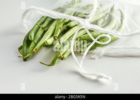 Fagioli verdi in una borsa a rete di prodotti alimentari sostenibile. Verdure in imballaggi riutilizzabili ecologici su sfondo chiaro. Zero sprechi shopping, senza plastica. Foto Stock