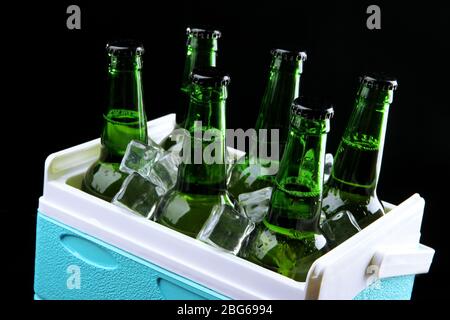 Bottiglie di birra con cubetti di ghiaccio in mini frigorifero, su fondo nero Foto Stock