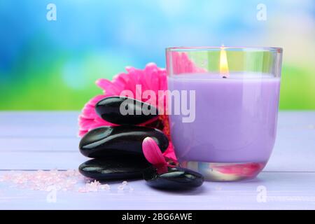 Pietre termali, bella gerbera e candela su tavolo di legno Foto Stock