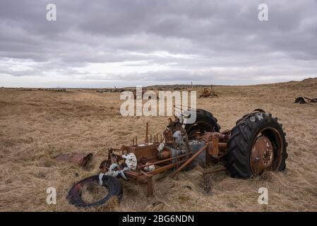 Resti di un trattore arrugginito si trovano abbandonati in un campo costiero, vicino a Hafnir, penisola di Reykjanes, Islanda Foto Stock