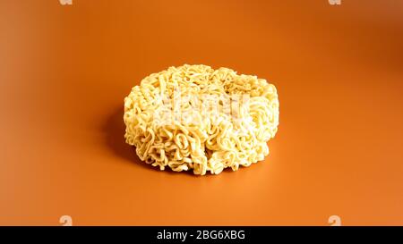 Pasta coreana istantanea a forma di cerchio su sfondo marrone. Vermicelli crudi, essiccati giallastro-bianchi, con lunghe linee rotonde e ritorti in dif Foto Stock