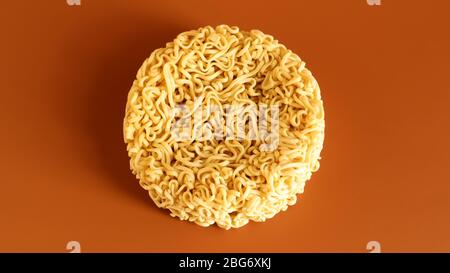 Pasta coreana istantanea a forma di cerchio su sfondo marrone. Vermicelli crudi, essiccati giallastro-bianchi, con lunghe linee rotonde e ritorti in dif Foto Stock