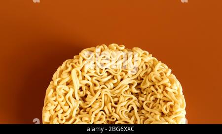 Pasta coreana istantanea a forma di cerchio su sfondo marrone. Vermicelli crudi, essiccati giallastro-bianchi, con lunghe linee rotonde e ritorti in dif Foto Stock