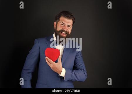 Assistenza sanitaria. Decorazione di giorno di San Valentino. Tuxedo uomo con cuore rosso. Festa di festa. Concetto di amore. Giornata mondiale del cuore. Brutale hipster barbuto in abito formale. Uomo d'affari in cravatta di prua. Attacco di cuore. Foto Stock