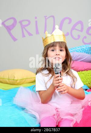 Bambina seduta sul letto con microfono in camera su sfondo grigio parete Foto Stock