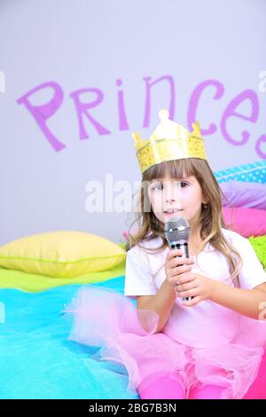 Bambina seduta sul letto con microfono in camera su sfondo grigio parete Foto Stock